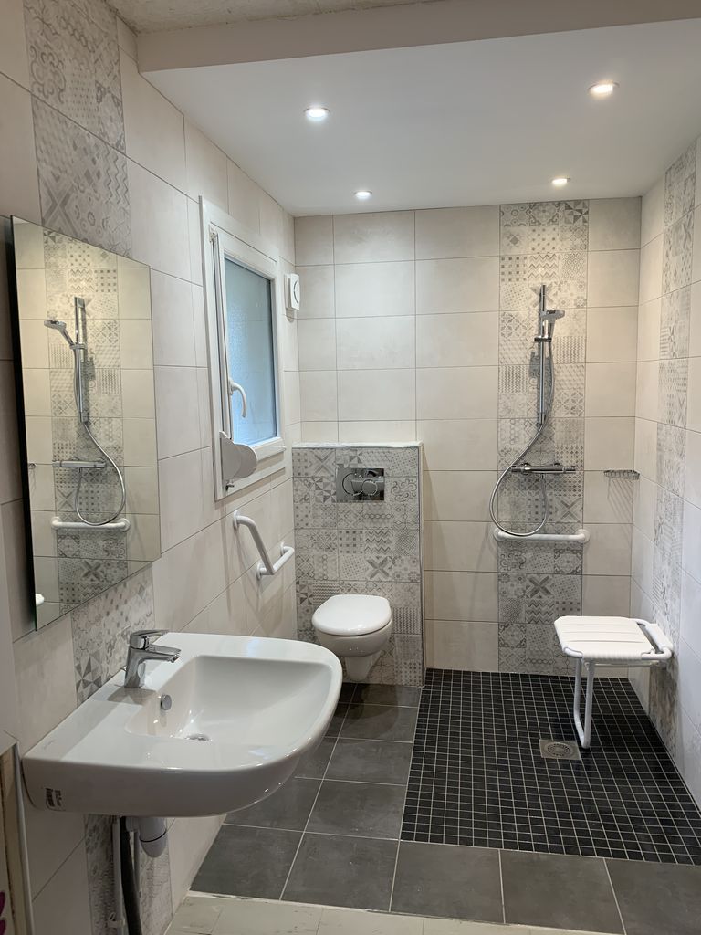 salle de bain PMR avec douche accessible, barres d’appui et siège de douche